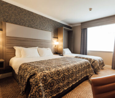 Spacious hotel room with cosy double and single beds, patterned bedding, soft lighting, and textured wallpaper.