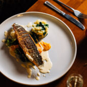 Elegant hotel dining with grilled fish, creamy sauce, and potato mash, with festive decor on a wooden table.