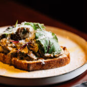 Gourmet open sandwich with fresh greens and grated cheese on a stylish plate in a cosy hotel restaurant setting.