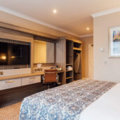 Elegant hotel room with king bed, large TV, and workspace; warm lighting and serene art create a cosy atmosphere.